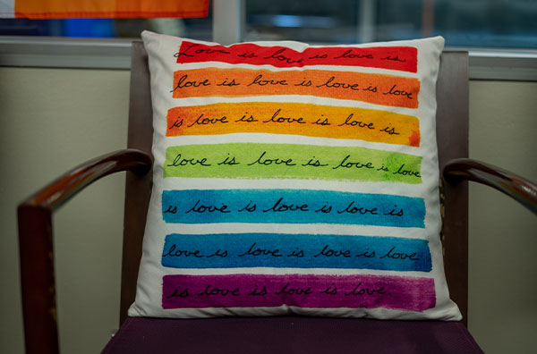 Throw pillow sitting on a chair with "love is love" written on a rainbow background
