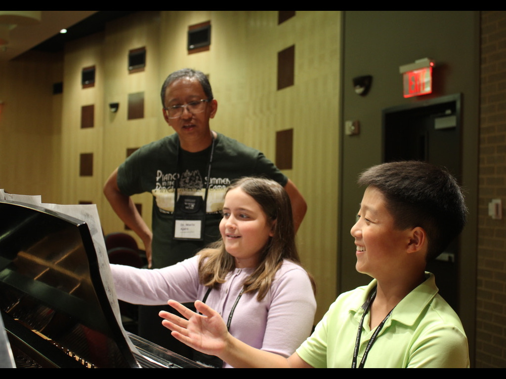 Two piano students enjoy hands-on coaching by a faculty member 