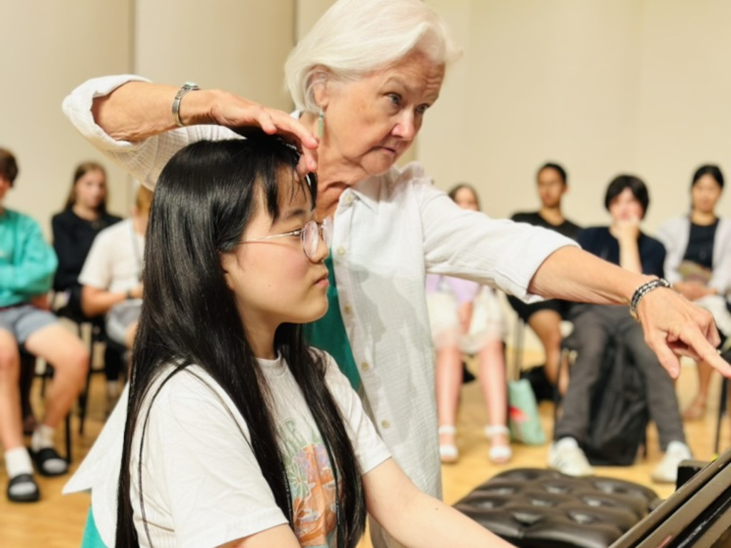 A faculty member works with a piano student on posture