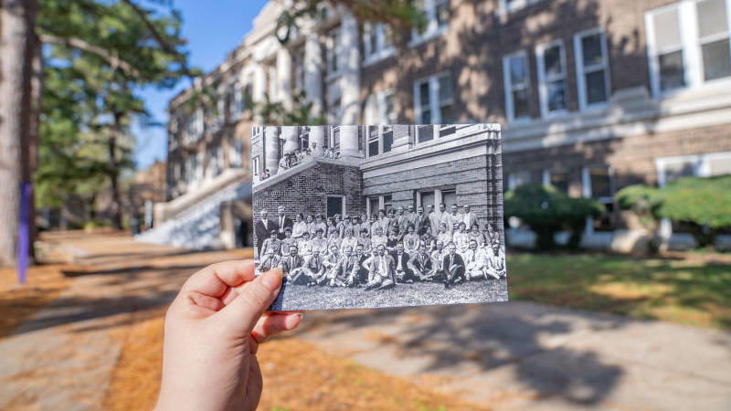 A vintage black and white photo is held in front of the modern-day Austin building