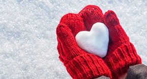 person wearing red mittens in the snow holding a heart-shaped snowball