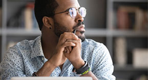 man with folded hands looking out the window deep in thought