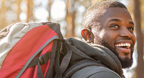 young man with a bacpack in the woods, smiling