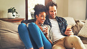 a man and woman sitting on a couch smiling and looking at an Iphone together