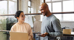 woman at laptop smiling at man holding a cell phone