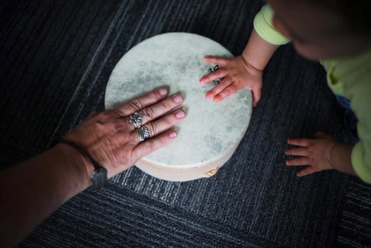 hand of an adult and the hand of a child on a small drum
