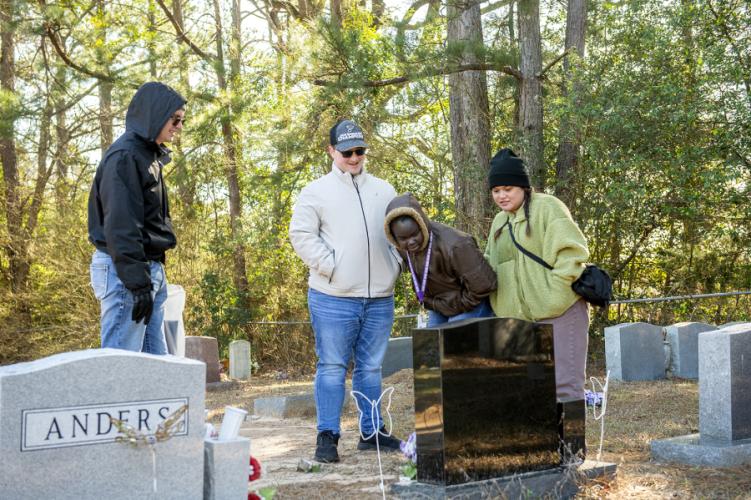 Four Stephen F. Austin State University students who joined the tour study a gravestone at the Sand Hill Cemetery near Chireno.