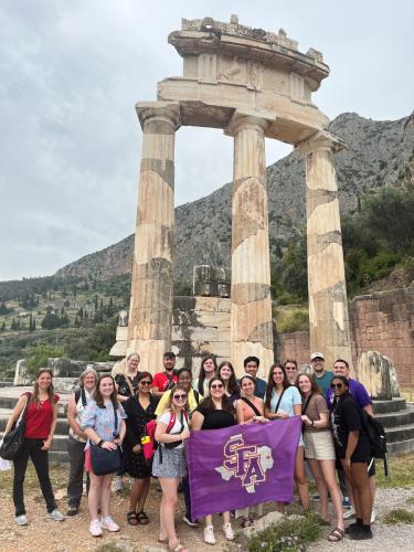 Students from various colleges and areas of study at Stephen F. Austin State University pose in front of a site in Delphi, Greece.