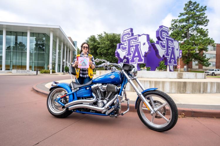 Katherine Noble poses behind her motorcycle with her book, "If You Give a Girl a Motorcycle."
