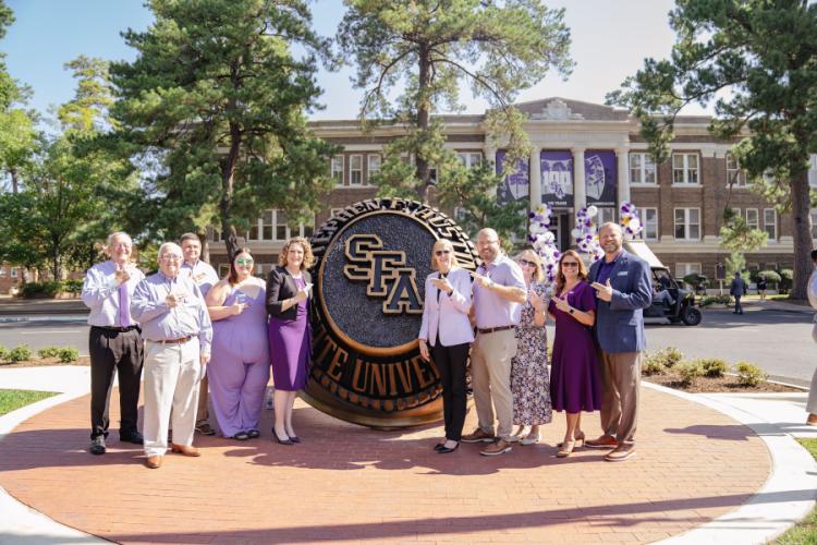 Board members for Stephen F. Austin State University’s Alumni Association pose in front of the SFA ring statue during the Centennial Ring Plaza dedication event Monday. 