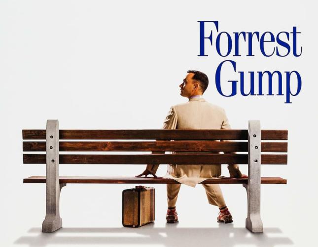 Forrest Gump promotional photo of Forrest Gump (played by Tom Hanks) seated on a woode bench alone with a suitcase