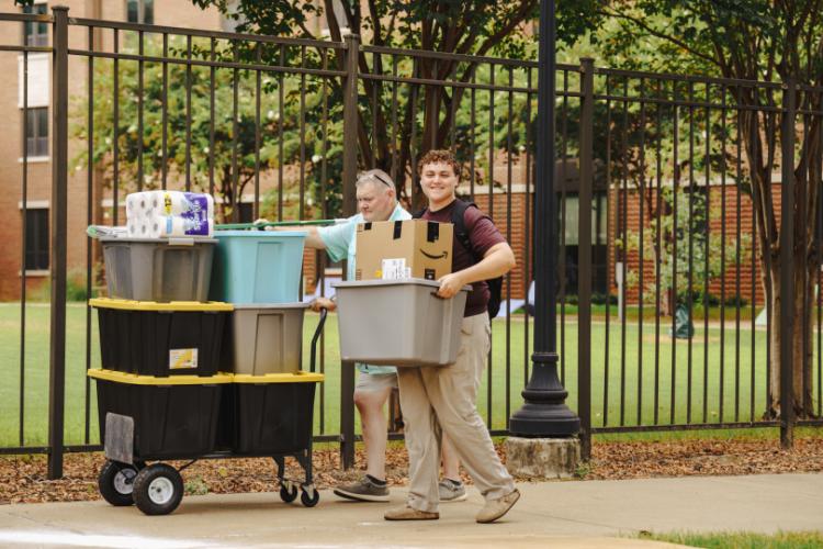 An SFA student carries a box of move-in supplies, while a family member assists with a cart.