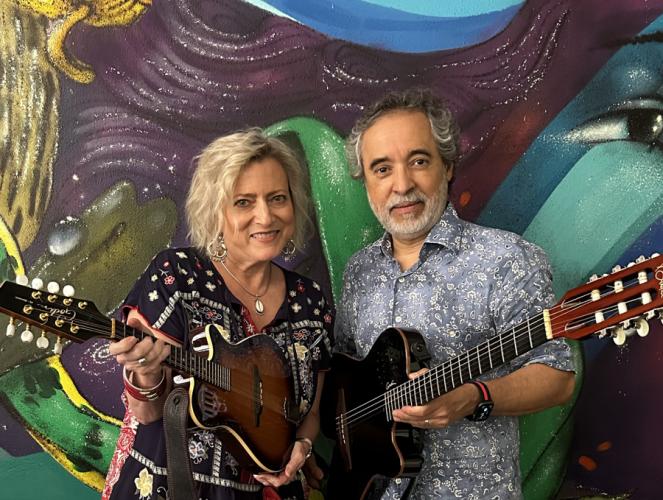 Drs. Jeana Paul and Juan Carlos Ureña hold instruments in front of a colorful wall mural