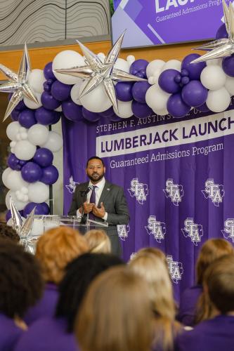 Dr. Kent Willis speaks about the Lumberjack Launch program to a large crowd with a backdrop of purple and white balloons