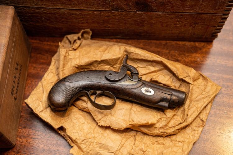 A derringer pistol from the 1800s rests on a brown, wrinkled paper bag
