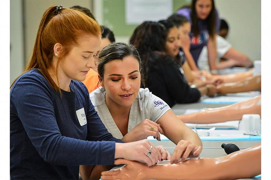 Loren Tezanos helping Maci Mitchell insert an IV into a mannequin arm