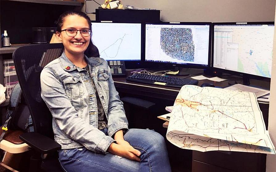 Female student sitting at a desk with monitors of maps 
