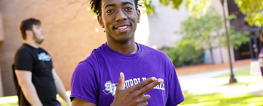 student in Purple Haze shirt giving the "Axe 'em, Jacks" sign