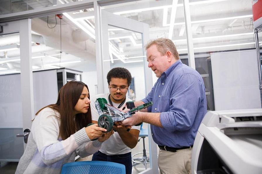 Instructor and students examining a mechanical device in a lab
