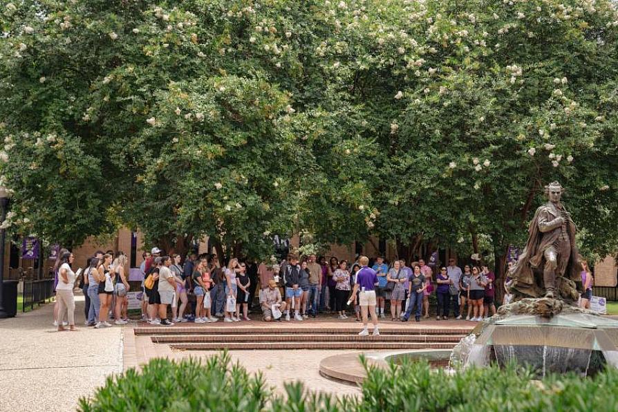 Tour group gathered near a statue and trees on a college campus