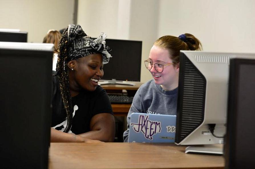 two smiling students working together at a laptop
